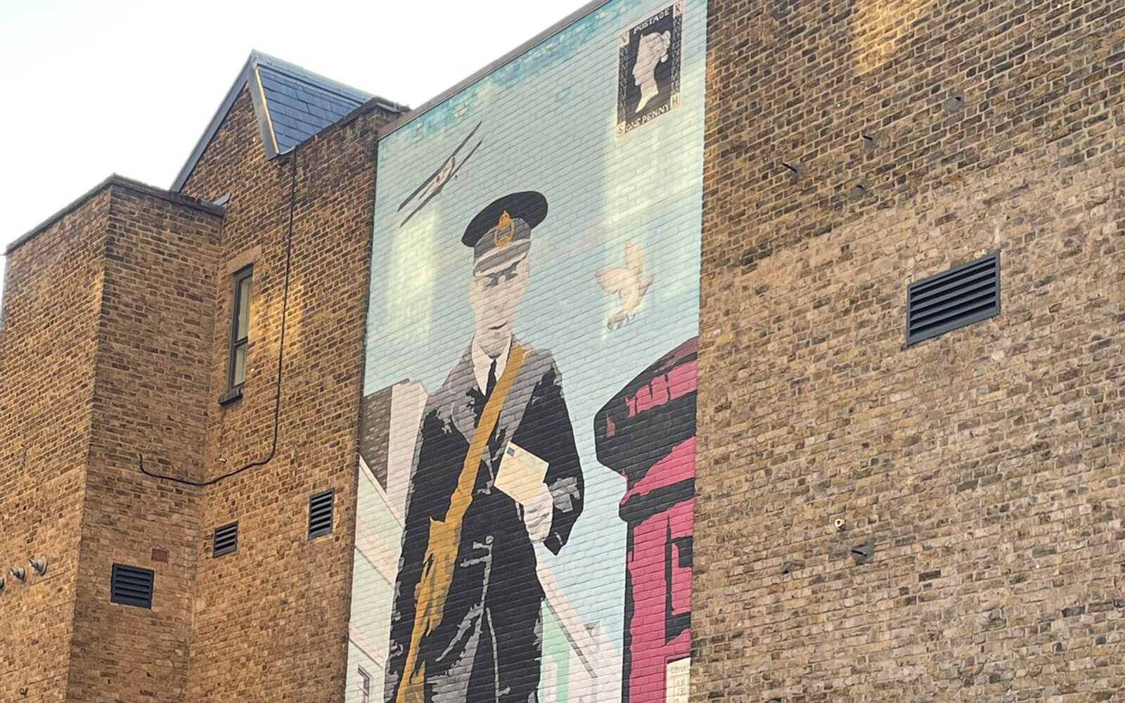 Mural of a postman painted on the side of The Postal Museum building