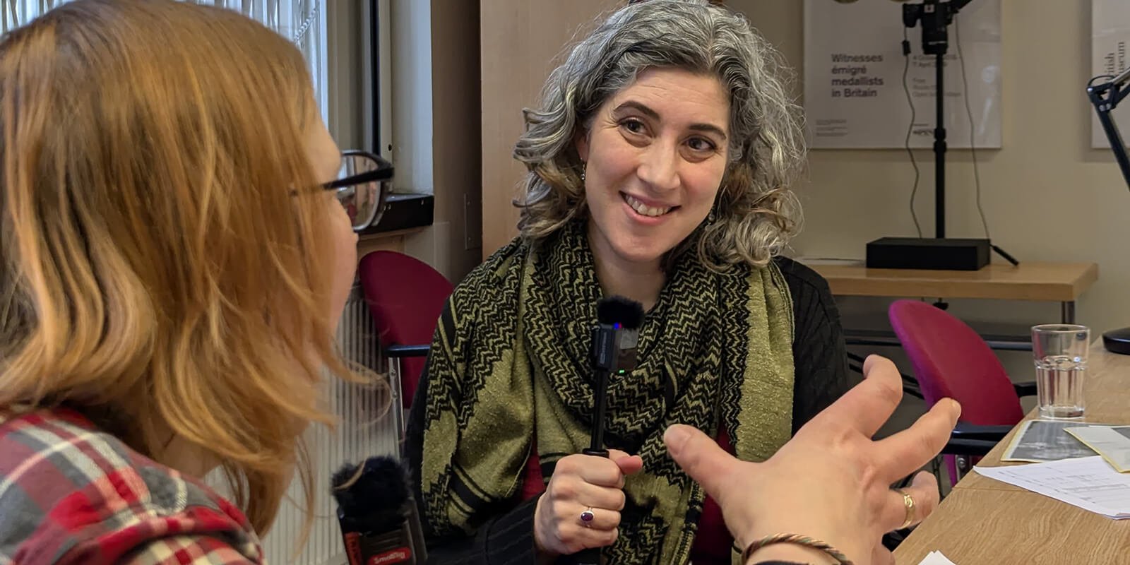Two people sat at a desk with microphones. In front of them are pictures of coins from the Chew Valley Hoard