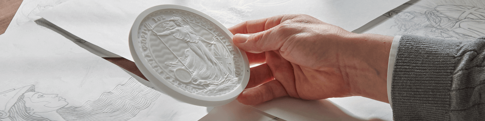 A picture of a man's hand holding a plaster model against a background of sketches and drawings