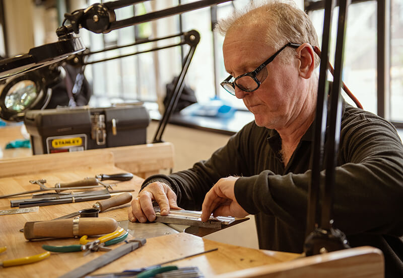 A man at a work bench with lots of tools making delicate gold jewellery