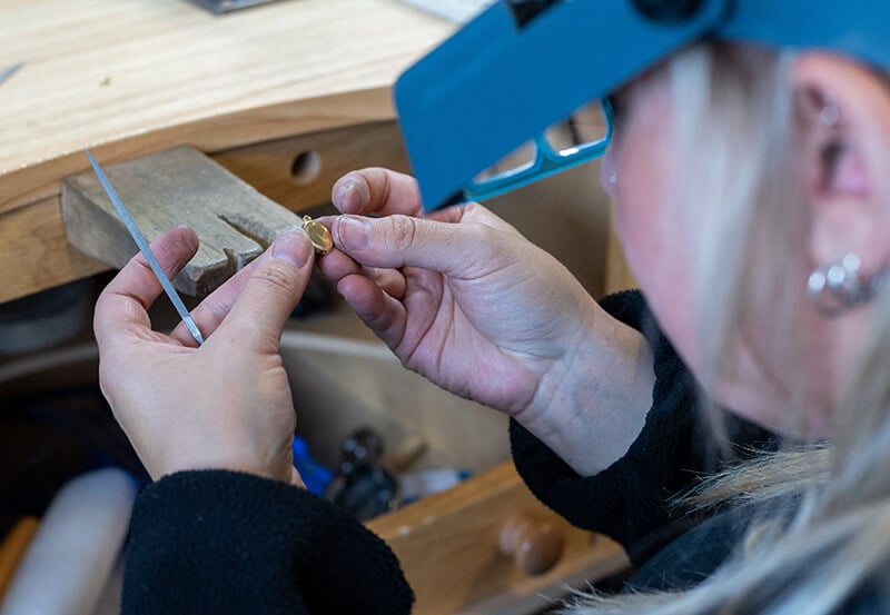 A woman sat at a work bench making small gold jump rings for jewellery