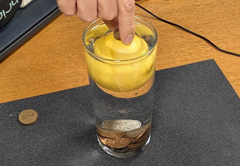 A member of the Museum team playing a game in which the player must balance a coin on a lemon suspended in a glass of water