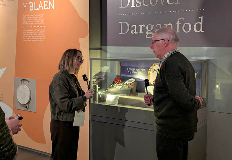 Photograph of Royal Mint Museum Exhibition manager Abigail Kenvyn interviewing Bob Meggs in front of an exhibition of his mother's maundy collection.