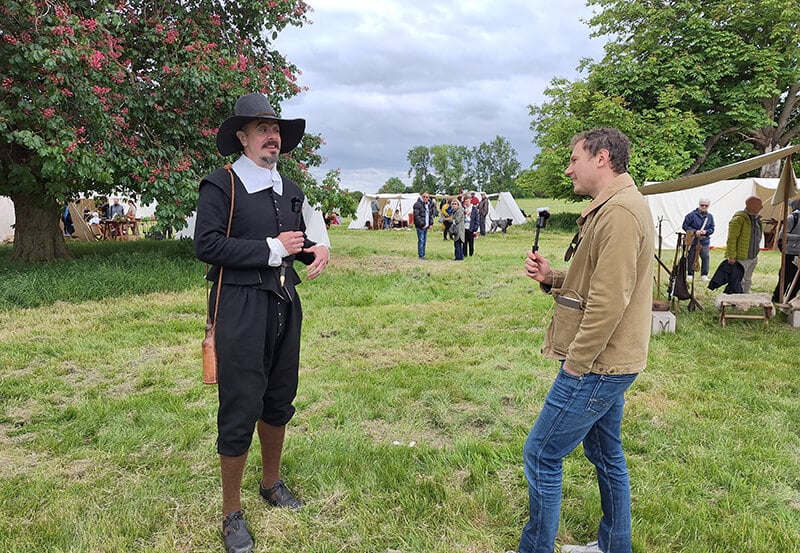 Chris Barker standing in a field interviewing a member of the Sealed Knot society in character as a parliamentarian preacher
