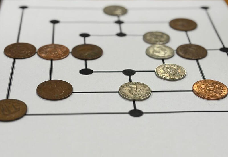 A piece of paper with dots and squares printed on for the game 'Merels' or 'Three Man's Morris'. Pre-decimal coins are being used as counters
