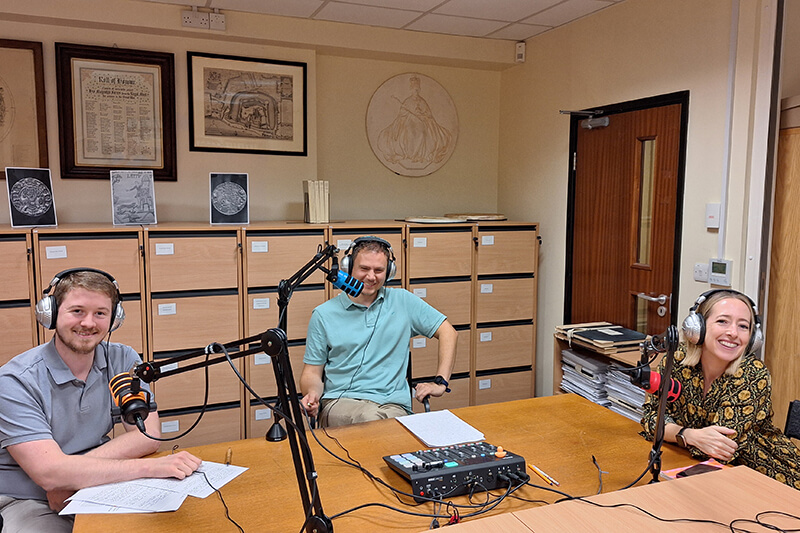 The members of the podcast crew in the studio with headphones and recording equipment
