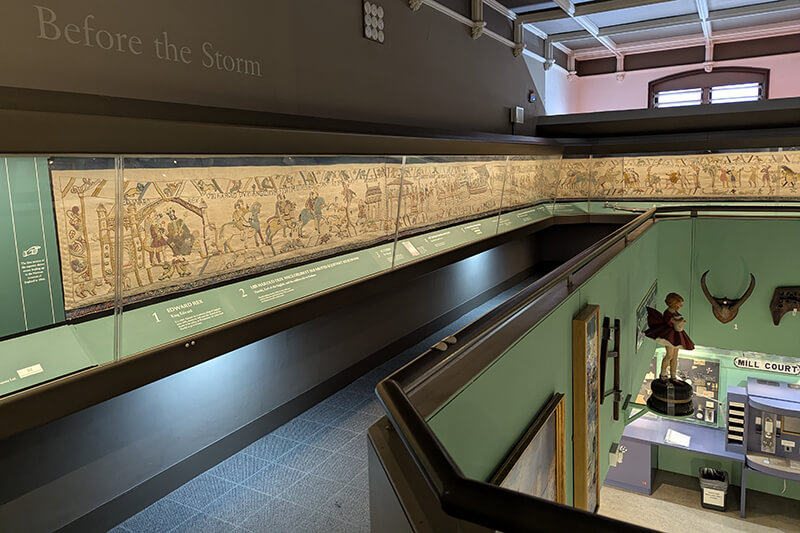 A dark two level gallery at Reading Museum displaying part of a full sized replica of the Bayeux Tapestry