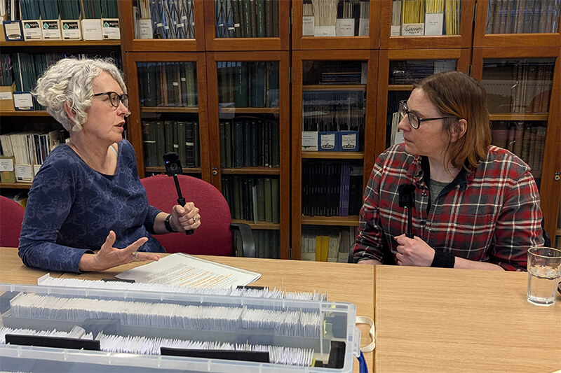 Wendy Scott and Susan Sandford talking into microphones while sat behind a table with papers on
