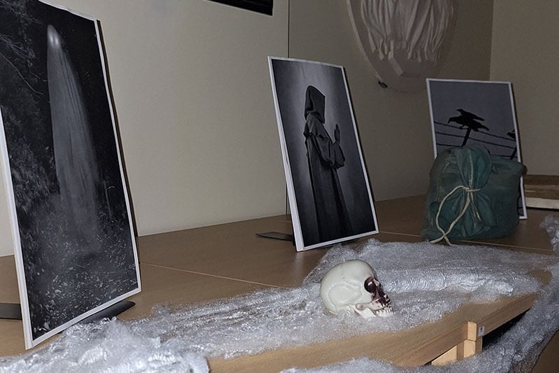In a dark room, filing cabinets have pictures of ghosts and ravens laid out on top, along with fake spider webs and old looking bags of money